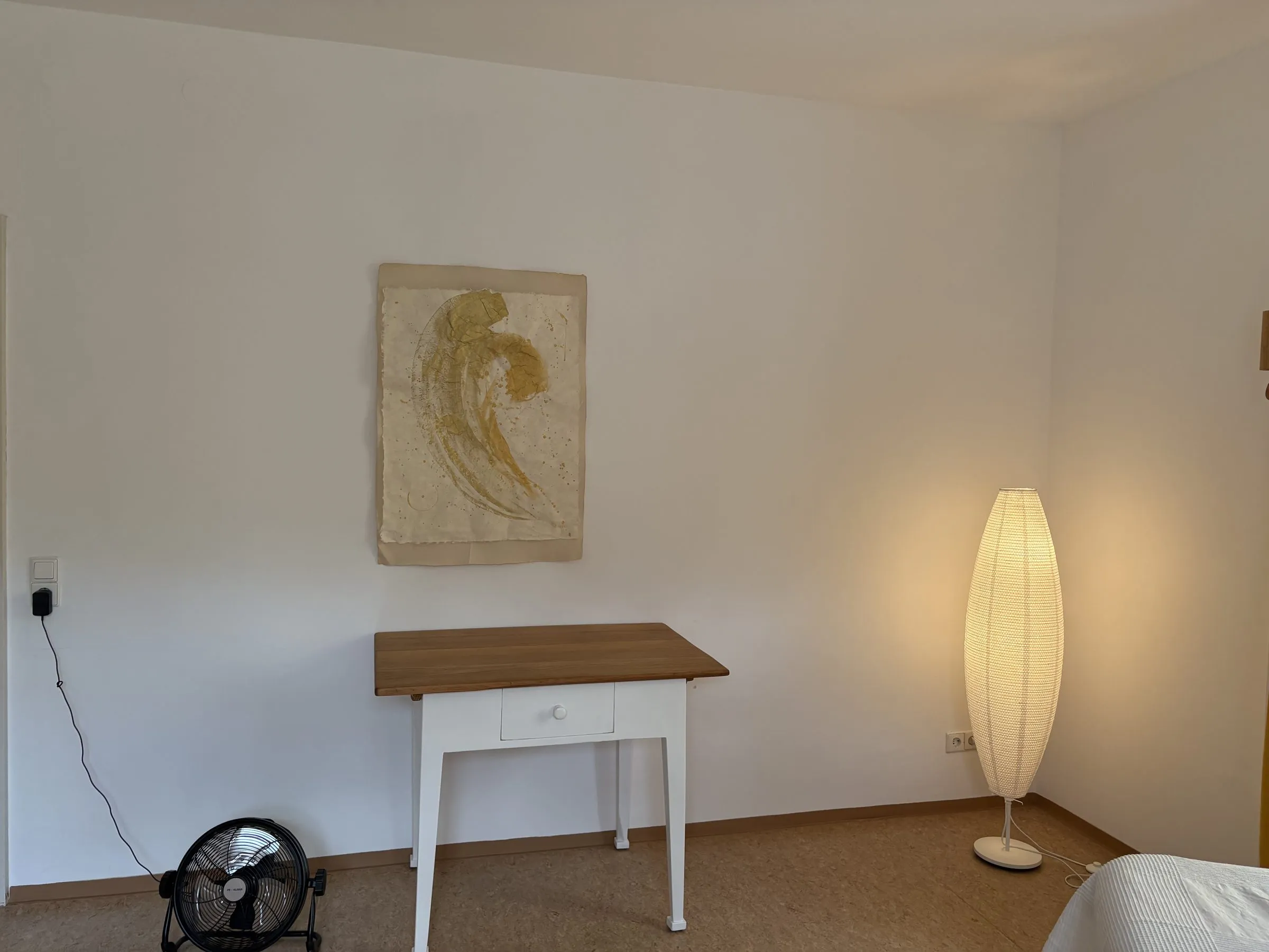 Heller Praxisraum mit einem Bild auf Büttenpapier, kleinem Holztisch und warmer Stehlampe